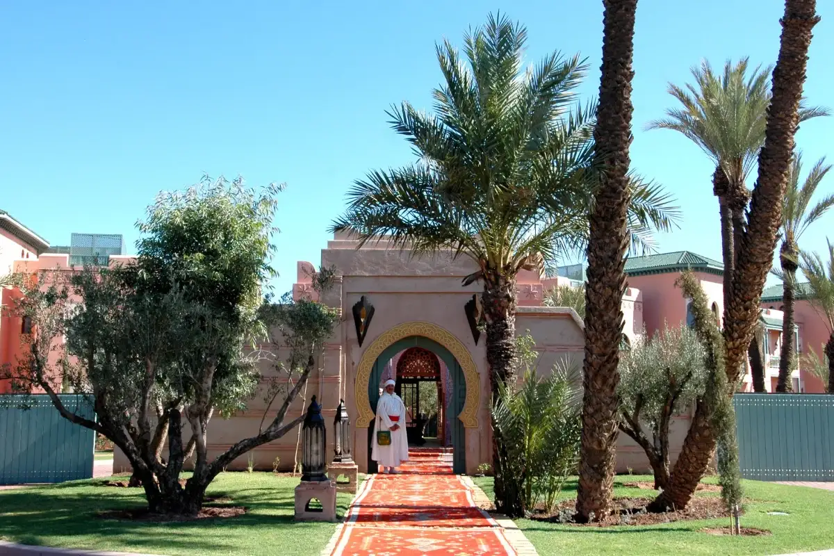 The front entrance archway of a typical luxury resort surrounded by palm trees in the Marrakech Palmeraie district.