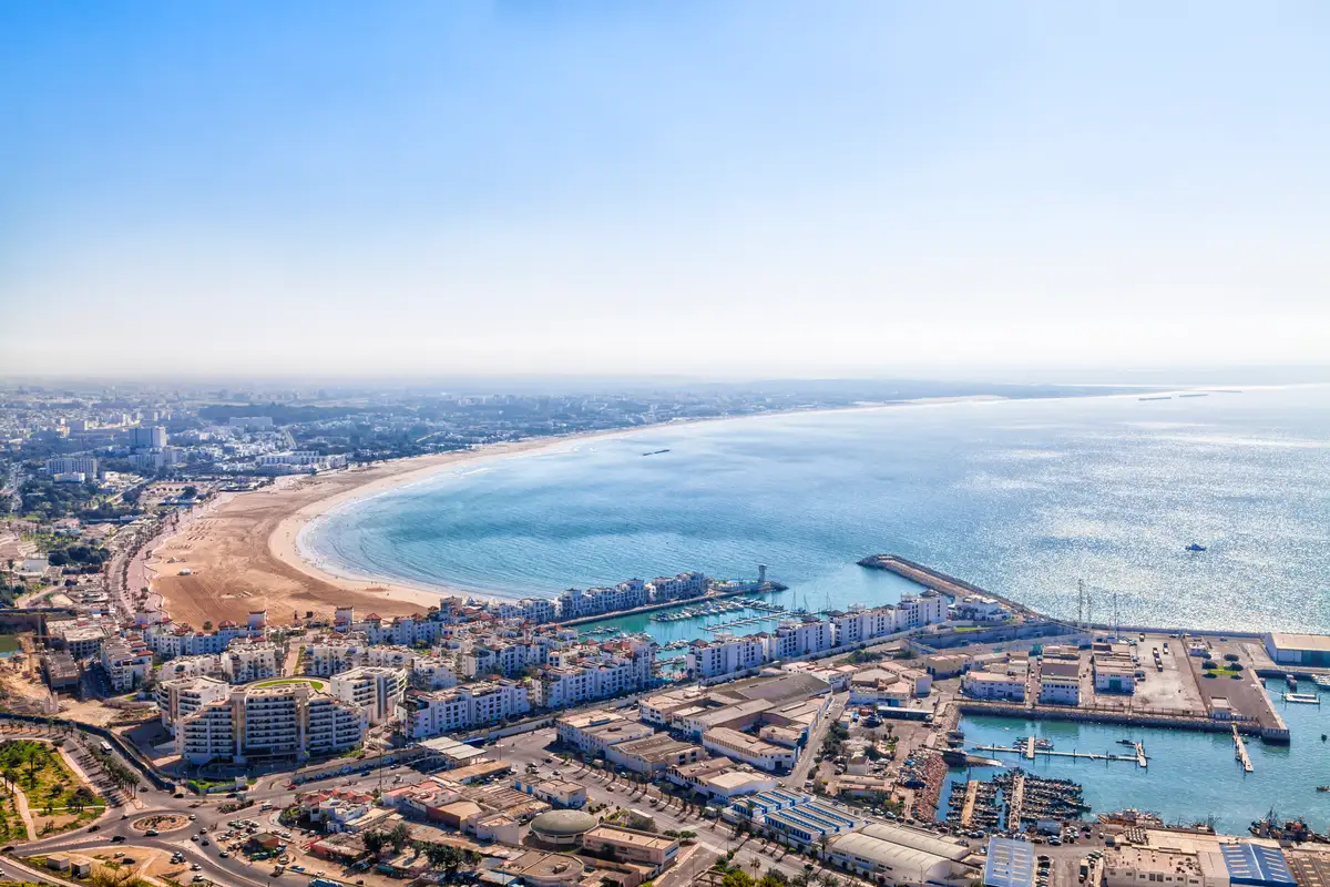 A sweeping hilltop view of Agadir Bay, featuring the expansive sandy beach, the Atlantic Ocean, and the Agadir marina, where your direct private transfer to Marrakech begins.