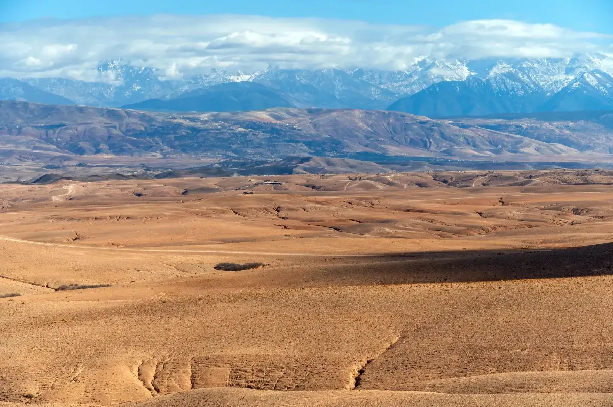An expansive view of the Agafay desert featuring rugged rocky terrain and stunning distant mountains under a clear blue sky.