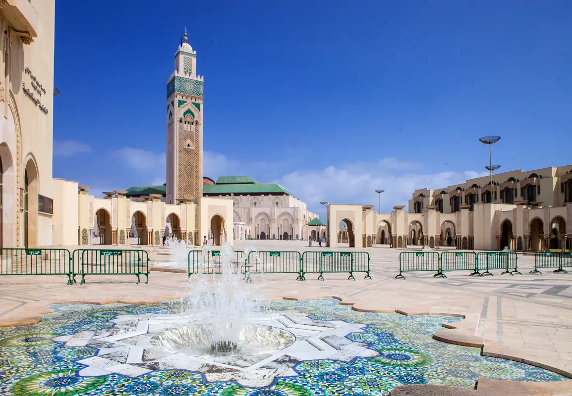 The iconic Hassan II Mosque in Casablanca featuring its minaret tower and beautiful foreground shallow pools with small fountains and blue mosaics.